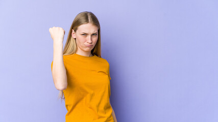 Young blonde woman isolated on purple background showing fist to camera, aggressive facial expression.