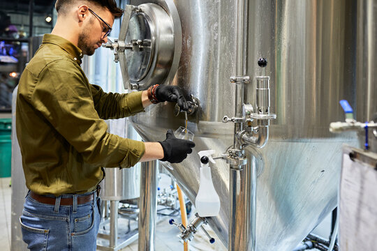 Man Working In Craft Brewery Tapping Beer From Tank