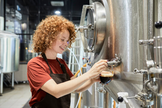 Woman working in craft brewery tapping beer from tank