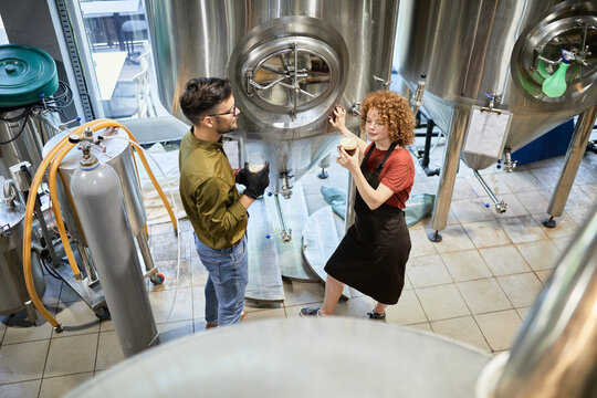 Man and woman working in craft brewery checking quality of a beer