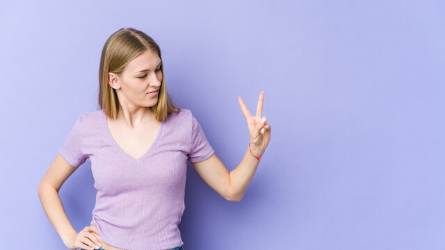 Young blonde woman isolated on purple background joyful and carefree showing a peace symbol with fingers.