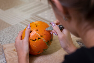 the process of making a Halloween pumpkin. cutting out the mouth by brunette girl. horror theme and Hallowe'en. 