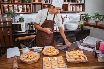 A professional male chef with a mobile phone prepares a donut order holding a digital tablet to in the kitchen