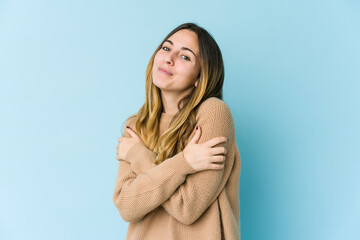 Young caucasian woman isolated on blue background hugs, smiling carefree and happy.