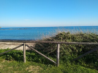 Fototapeta na wymiar Peaceful view of green grass, sandy beach and blue water at Nora beach near Pula in Sardinia, Italy