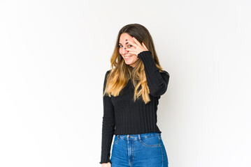 Young caucasian woman isolated on white background blink at the camera through fingers, embarrassed covering face.