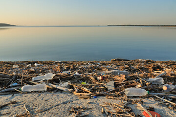 Landscape of polluted with plastic garbage shore of the lake on the sunset. Environmental disaster...