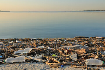 Landscape of polluted with plastic garbage shore of the lake on the sunset. Environmental disaster...
