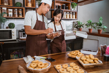 Fototapeta na wymiar Asian male chef shows partner donut order book, marketing homemade donuts