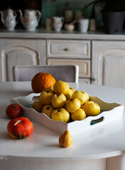 Yellow quinces in a white platter on a white table with orange pumpkins, autumn, fall concept