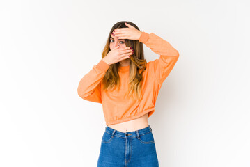 Young caucasian woman isolated on white background blink at the camera through fingers, embarrassed covering face.