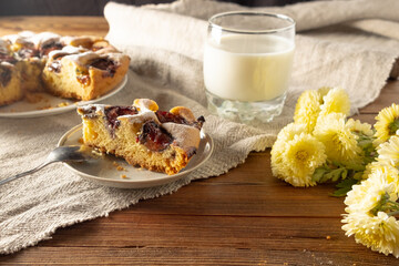 Plum cake and a glass of milk on the table, next to it are autumn chrysanthemum flowers. Homemade baking concept.