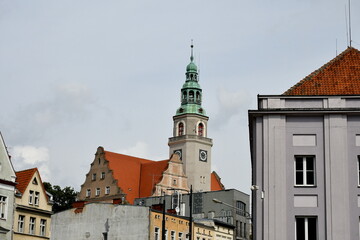 View of a tall tower of the town hall of a Polish city surrounded with block of flats and other habitable units seen on a warm yet cloudy summer day in the middle of a Polish square