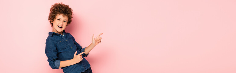 panoramic concept of excited curly boy in denim shirt pointing with fingers on pink