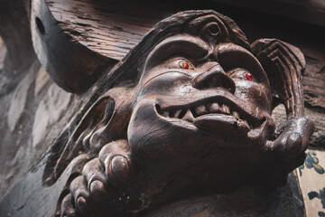 Medieval gargoyle with red eyes, close up. Demon figure with scary smile. Smiling wooden gargoyle...