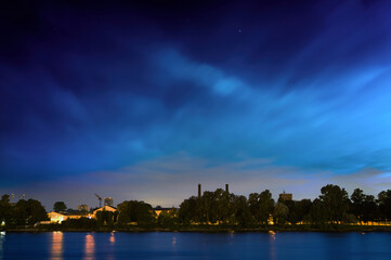 Starry sky with floating clouds over the city park with trees.