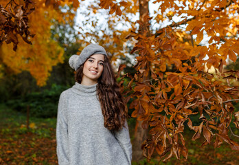Attractive stylish girl with curly hair walking in park dressed in warm grey autumn trendy fashion, wearing beret hat.