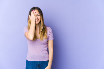 Young caucasian woman isolated on purple background having fun covering half of face with palm.