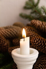 Christmas composition of a white candle in a white candlestick on a background of fir branches with cones