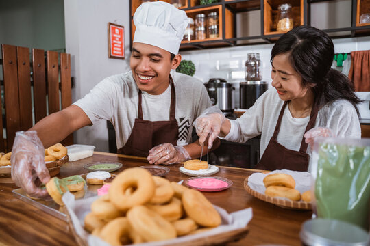 Smiling chefs couple dressed in aprons cooking together at the kitchen, making donuts