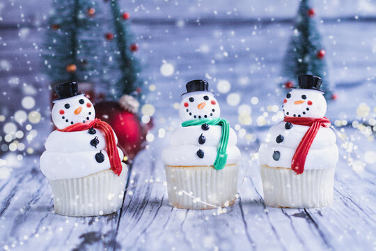 Three happy iced Christmas Snowman cupcakes with carrot nose, Santa hat, and scarf. Selective focus with blurred foreground and background.