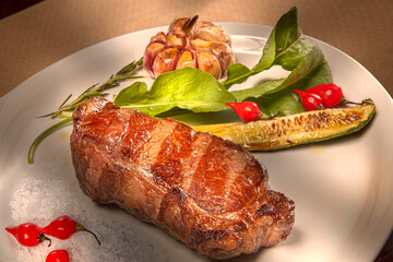 Juicy grilled rump steak with fried garlic and red pepper on a white plate