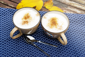 Two cups of cappuccino or latte with brown sugar and cinnamon. Coffee for two on a rustic table outside. Fall season beauty.