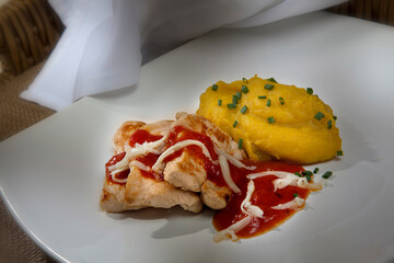 Grilled chicken fillets topped with tomato sauce and grated cheese and cassava puree on a white plate