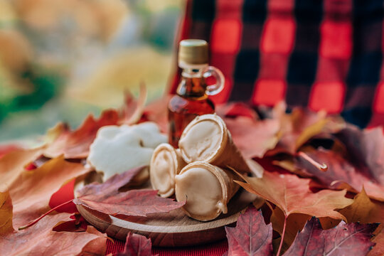Maple syrup taffy cones dessert with traditional bottle and plaid cloth table - red leaves on table. Quebec local food.