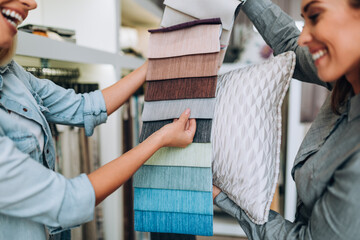 Young woman designer talking with a saleswoman and chooses fabrics for curtains in textile show...