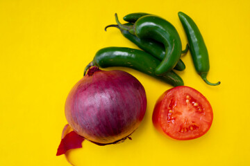 Green chilies, red onion and tomato on a yellow background