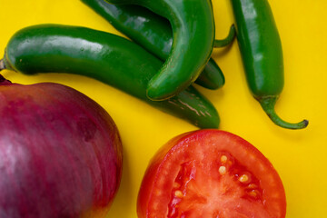 Green chilies, red onion and tomato on a yellow background