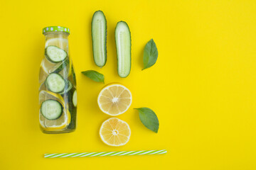 Top view of detox water with cucumber and lemon in a glass bottle on the yellow background