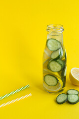 Detox water with cucumber and lemon in a glass bottle on the yellow background