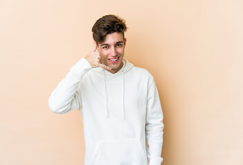 Young caucasian man isolated on beige background showing a mobile phone call gesture with fingers.