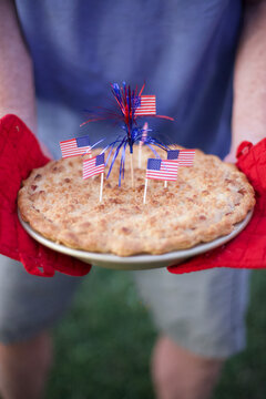 American Apple Pie with Flags Held by Two Hands with Red Gloves for 4th of July Patriotic Holiday