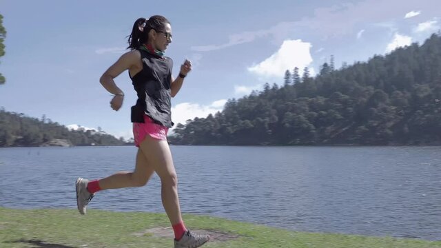 Mujer joven de trail running cerca de un lago al aire libre en la monta&ntilde;a, haciendo entrenamiento de resistencia. Estilo de vida saludable y disciplina deportiva