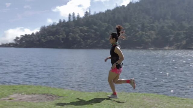 Mujer joven de trail running cerca de un lago al aire libre en la monta&ntilde;a, haciendo entrenamiento de resistencia. Estilo de vida saludable y disciplina deportiva