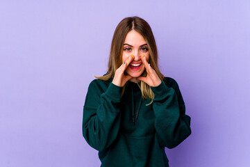 Young caucasian woman isolated on purple background saying a gossip, pointing to side reporting something.