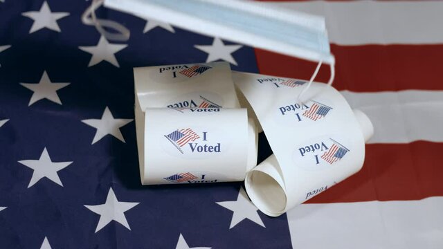 Face mask falling on stack of I Voted stickers for American elections on Usa flag.