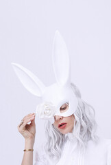 Young blonde girl in rabbit mask in stylish white minimal space. Fashion festive Christmas / New Year holidays party celebration concept.