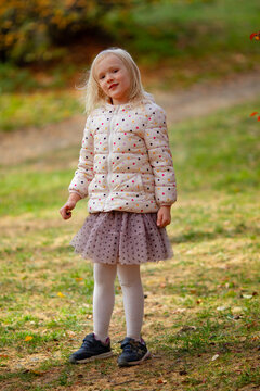 Adorable blond girl wearing fancy jacket and skirt in the park on a beautiful windy autumn day. 