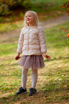 Adorable blond girl wearing fancy jacket and skirt in the park on a beautiful windy autumn day. 
