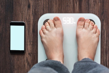 Top View Of a Person Standing On a Smart Weighing Scale and a smartphone connected to the Weighing...