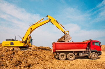 Fototapeta premium Excavator loads clay into the body of a dump truck on a sunny summer day
