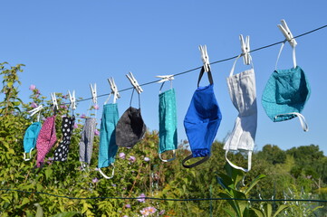 a lot of different self made corona face masks out of fabric hanging on a clothesline for drying