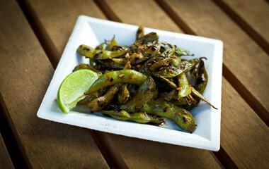 Square Plate of Edamame Pods on White Plate with Lime Wedge on Wooden Slat Table