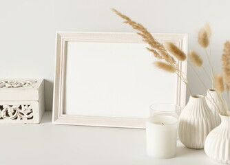 Photo frame mock up, fluffy reeds bouquet in a vase, interiour accessories near the white wall. Copy space template. Minimalist scandinavian interior design .