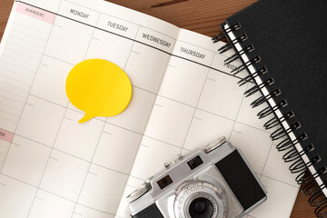Vintage camera, black notebook, blank diary and yellow post-it. Wood table. Top view.