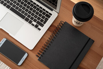 Work from home space: open laptop, coffee cup, black notebook and a mobile phone. Wood table. Top view. 